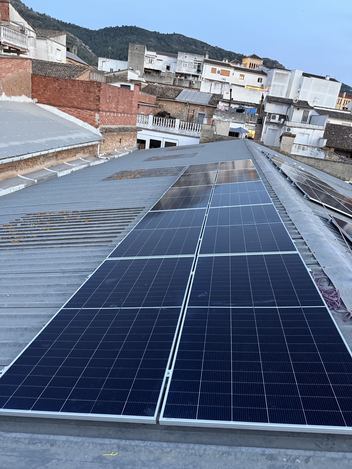 Hilera de placas sobre cubierta metálica, con el pueblo y la montaña detrás