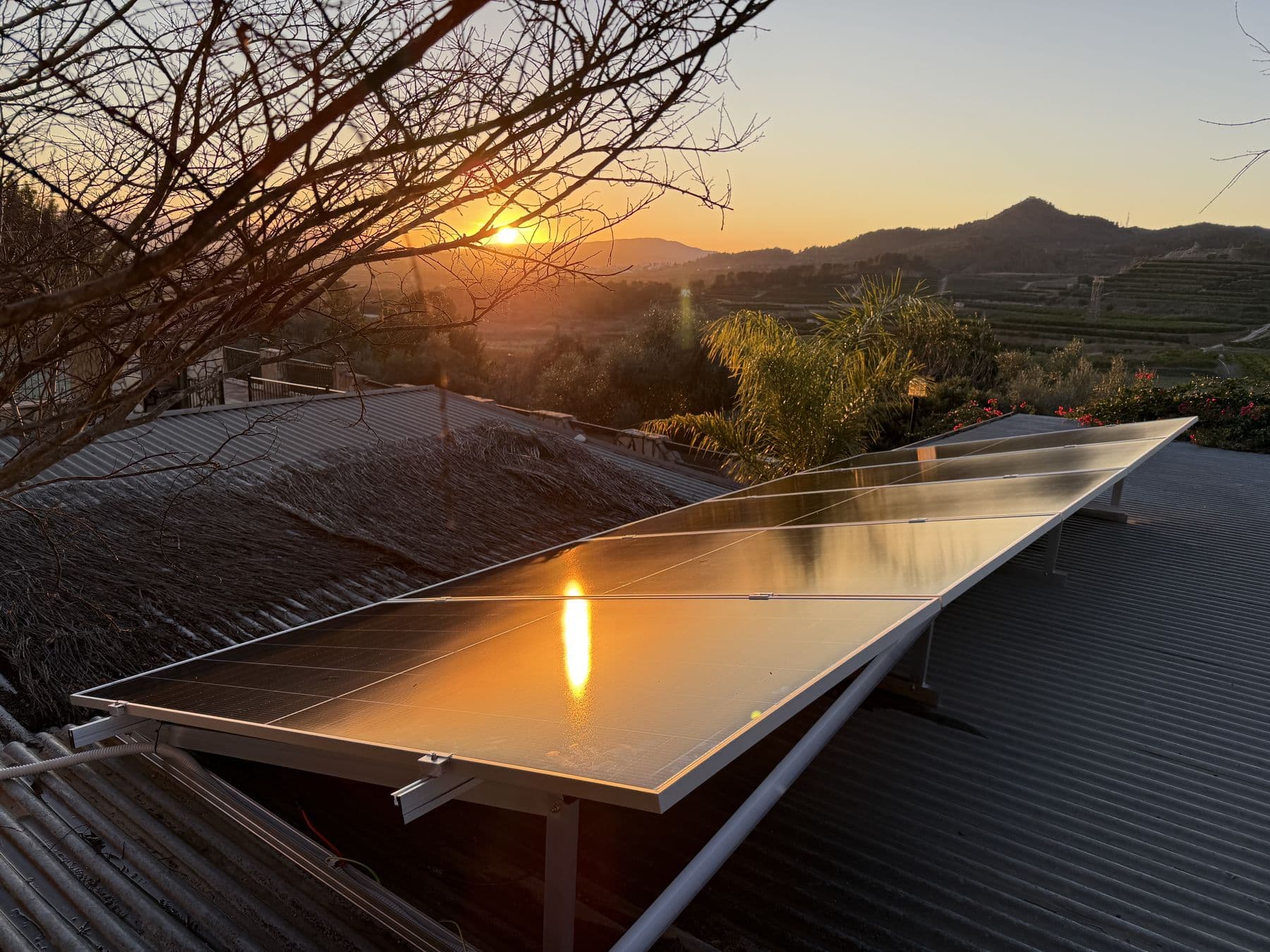 Placas solares al atardecer sobre una cubierta, con la sierra y los bancales al fondo